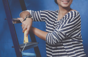 woman holding a paint roller while leaning on a ladder